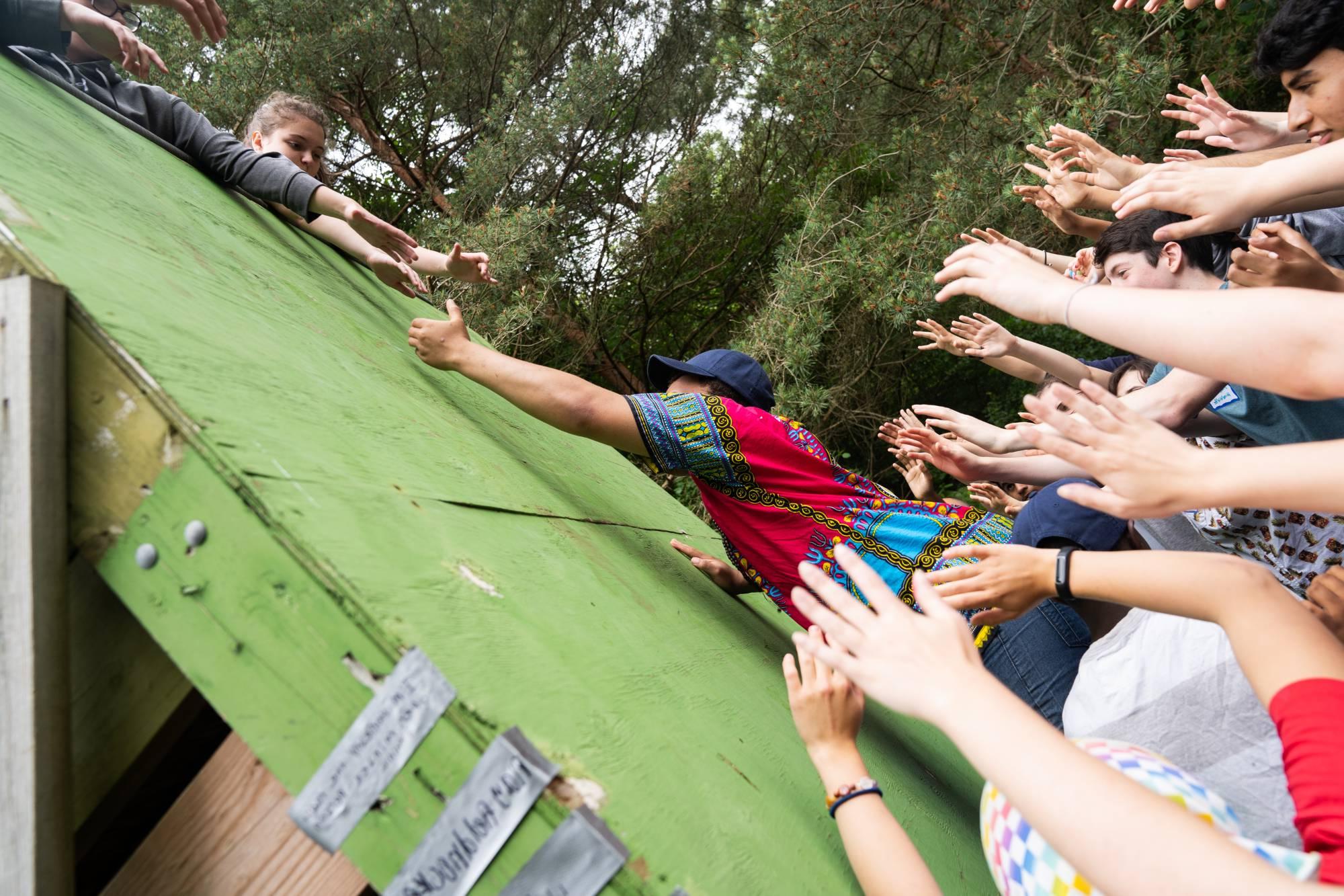 Students help each other scale wall on ropes course